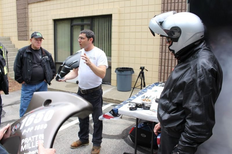 Motus Motorcycles president and co-founder Lee Conn (in white t-shirt)shows off some parts as Tom MacBurnie of Winsted, left, and Ernie Torizzo of Harwinton, right, listen. Bud Wilkinson / Republican-American 